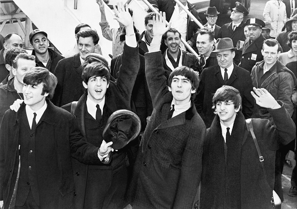 The Beatles wave to fans after disembarking a plane at Kennedy Airport.（出典 Wikimedia commons）
